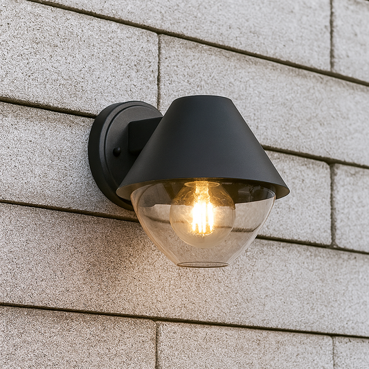 Schwarze Wandleuchte mit klarem Glasschirm und E27-Fassung, frontal fotografiert vor einer Hausfassade